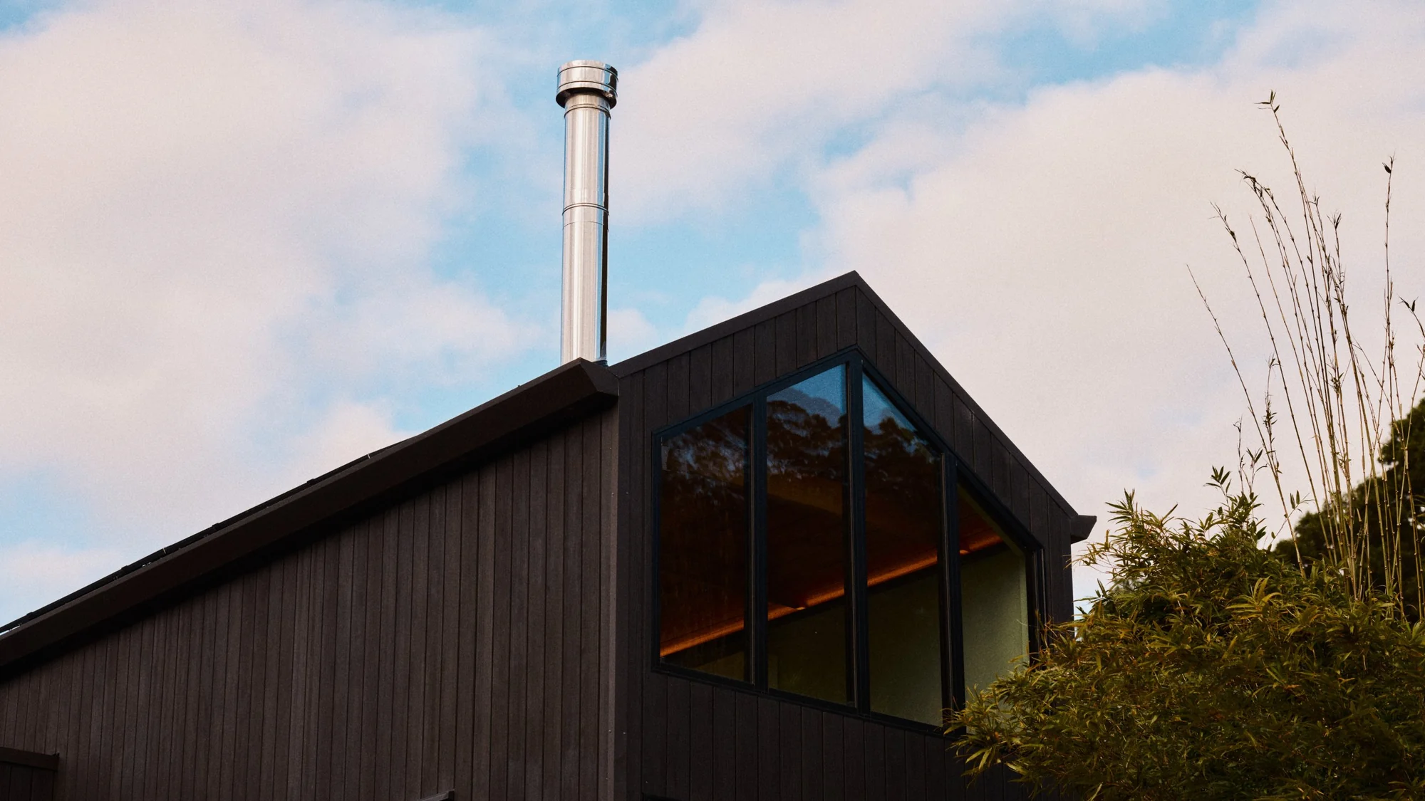 Dark vertical-board cladding and a raked gable window under a stainless steel flue, built by Amity