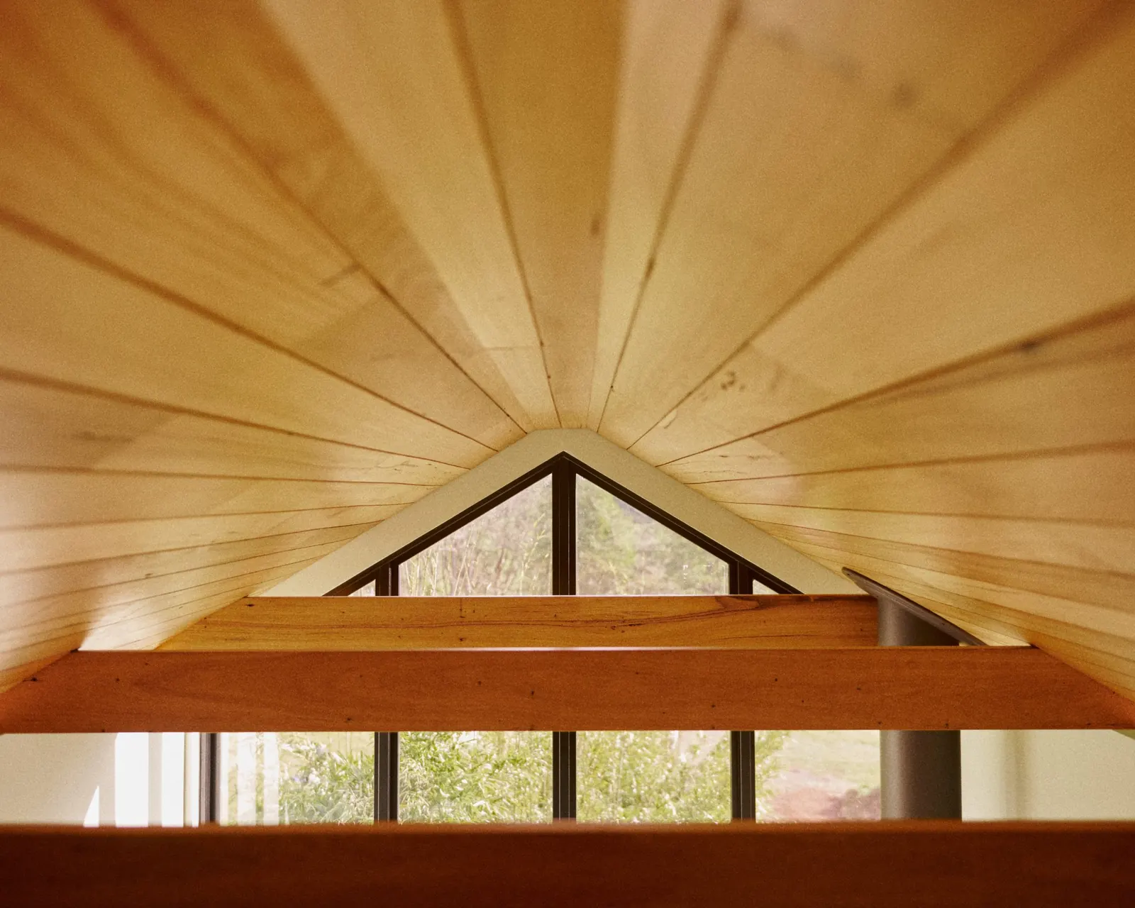 Inside an Amity-built cabin: timber-lined gable ceiling and exposed beams above a raked window