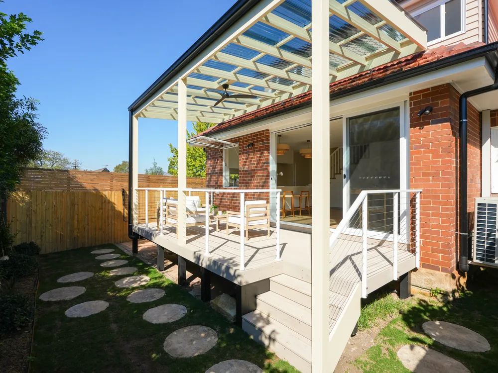 Covered rear deck under a polycarbonate pergola, with stepping stones to the garden