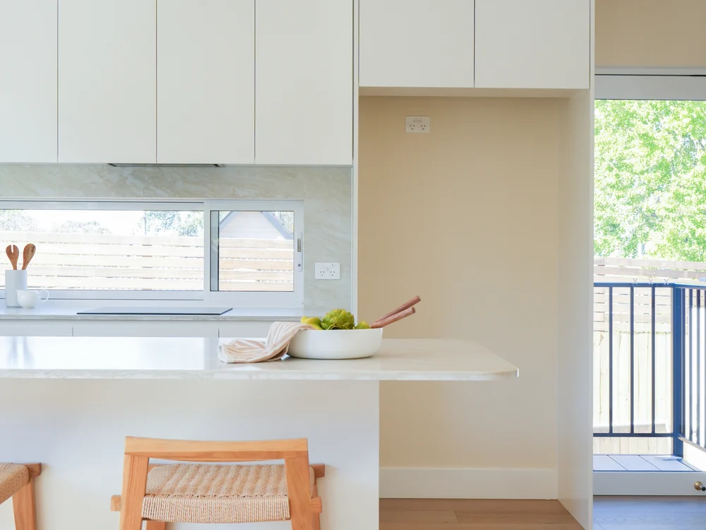 Kitchen island with a rattan pendant and woven bar stools, deck beyond