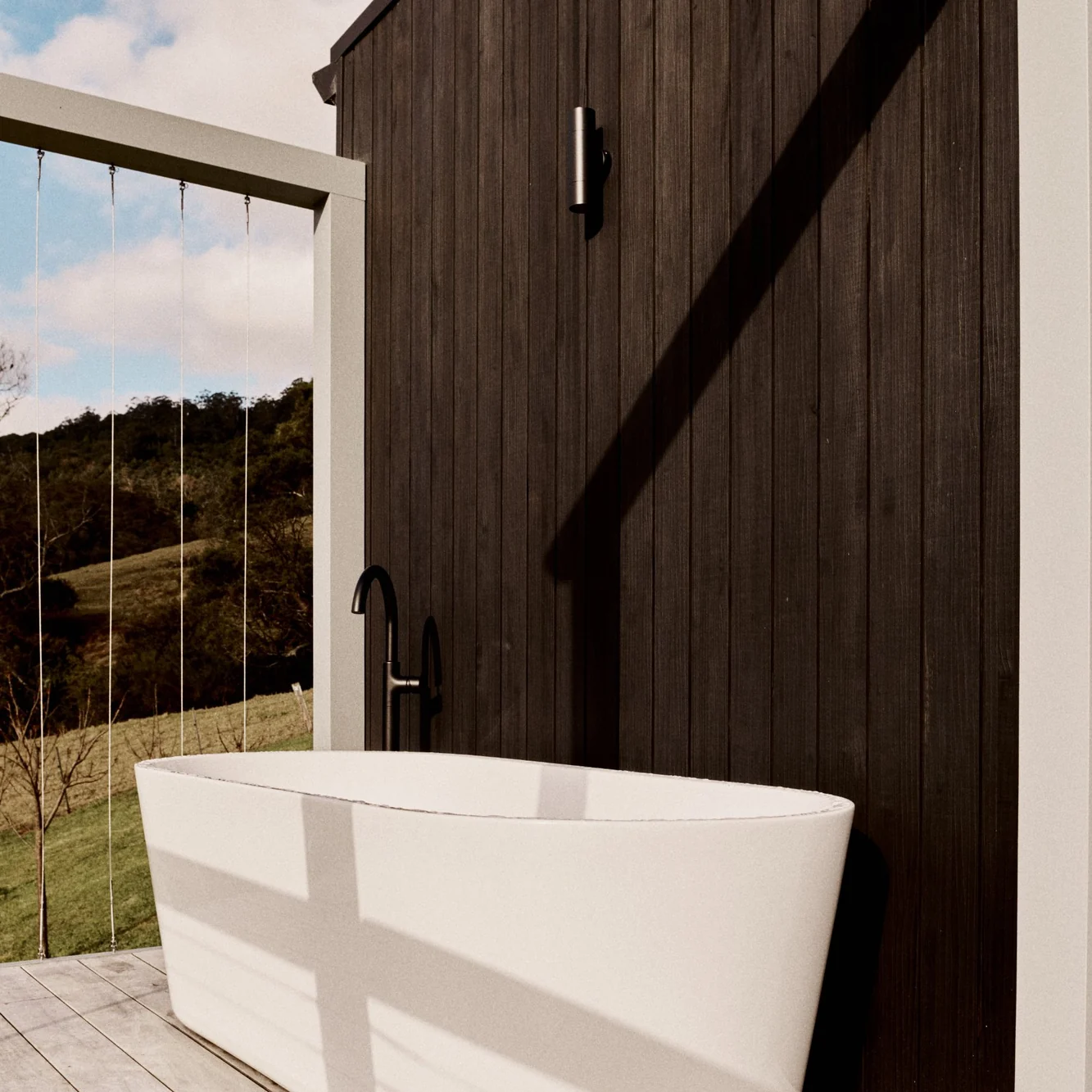 Freestanding bath on the deck against the charcoal cladding, the valley beyond