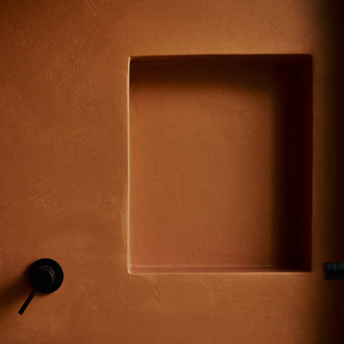 Terracotta-rendered shower wall with a recessed niche and a black mixer